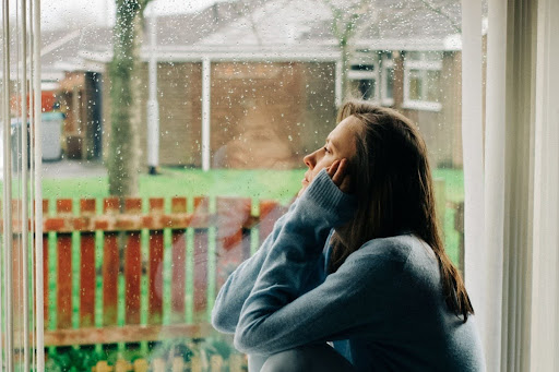 A woman with a sad expression looking out a window as it rains.