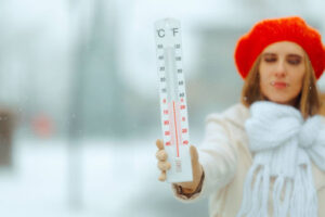A woman standing outside in the snow while holding a thermometer.
