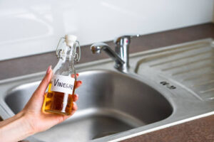 A hand holding a bottle of vinegar near a sink.