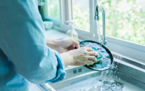 A person cleaning a plate in a kitchen sink with a sponge.