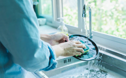 A person cleaning a plate in a kitchen sink with a sponge.