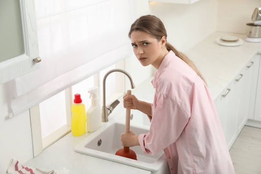 A woman plunging a kitchen sink.