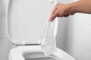 Someone holding a wet wipe over a toilet bowl.