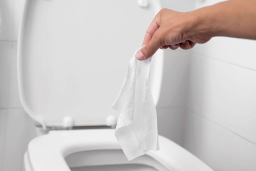 Someone holding a wet wipe over a toilet bowl.