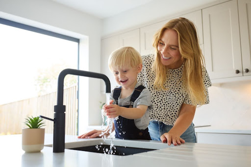 A woman and her son using a kitchen sink faucet.