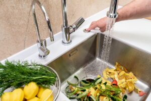 A sink full of food waste that is being put down the garbage disposal.